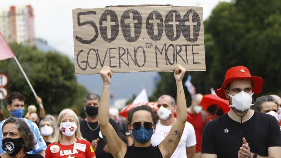 A woman wearing a protective face mask holds a sign with a message that reads in Portuguese; 