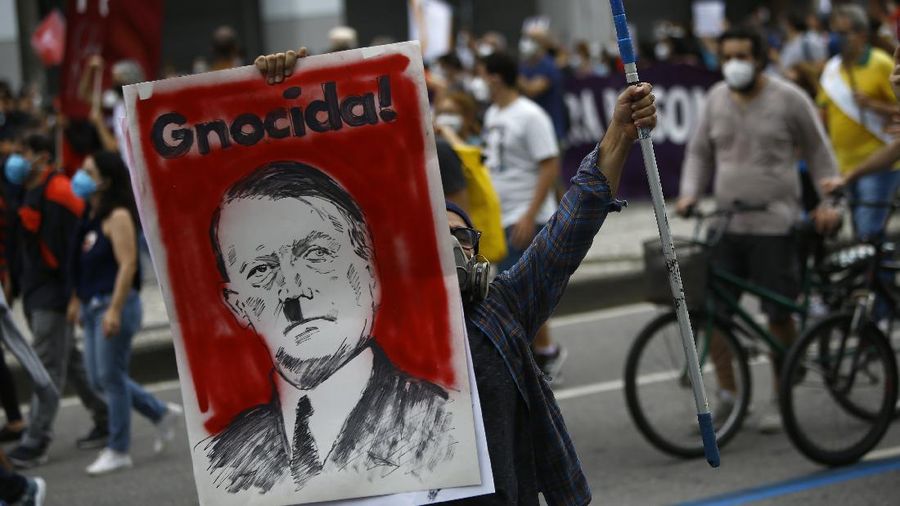 A protester holds a poster depicting Brazilian President Jair Bolsonaro as Adolf Hitler and the Portuguese word for genocidal, during a demonstration against Bolsonaro's handling of the coronavirus pandemic and economic policies protesters say harm the interests of the poor and working class, in Rio de Janeiro, Brazil, Saturday, June 19, 2021. Brazil is approaching an official COVID-19 death toll of 500,000 — second-highest in the world. (AP Photo/Bruna Prado)
