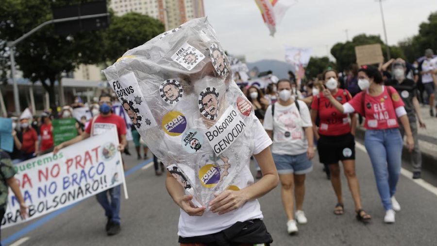 A woman wearing a protective face mask holds a sign with a message that reads in Portuguese; 