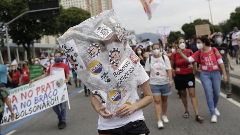 A woman wearing a protective face mask holds a sign with a message that reads in Portuguese; 