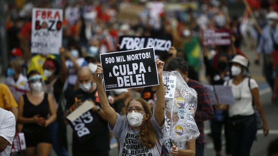 A woman wearing a protective face mask holds a sign with a message that reads in Portuguese; 