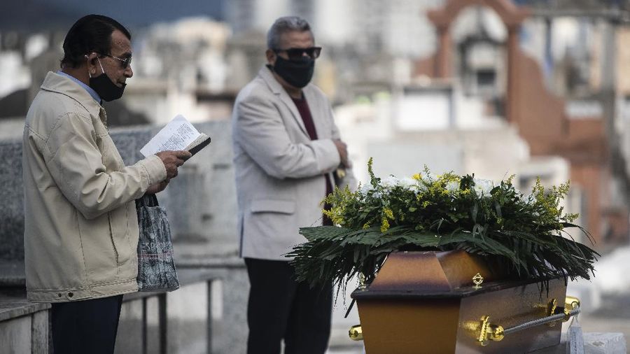 A woman wearing a protective face mask holds a sign with a message that reads in Portuguese; 