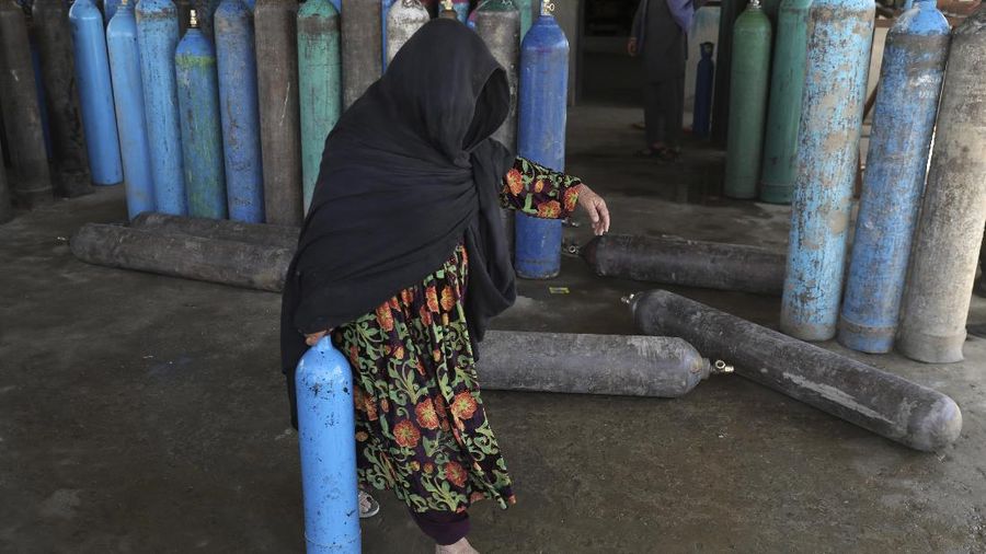 A woman carries an oxygen cylinder from a privately owned oxygen factory, in Kabul, Afghanistan, Saturday, June 19, 2021. Health officials say Afghanistan is fast running out of oxygen as a deadly third surge of COVID worsen. (AP Photo/Rahmat Gul)