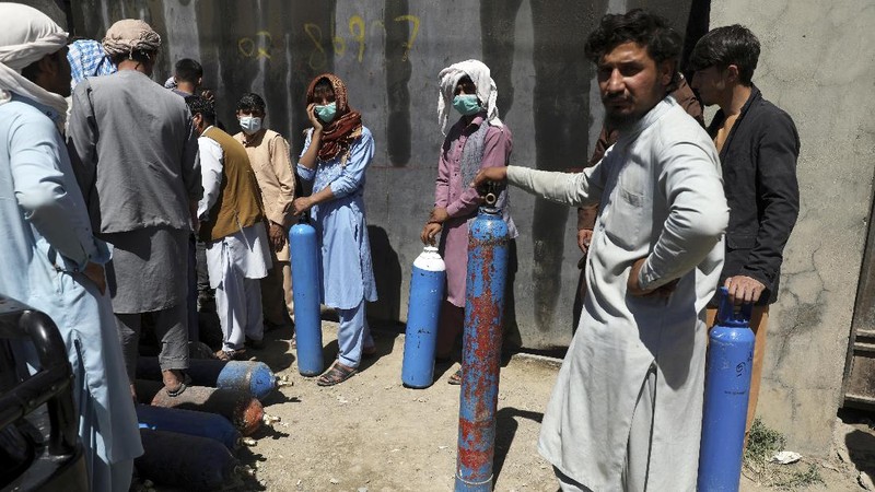 A woman carries an oxygen cylinder from a privately owned oxygen factory, in Kabul, Afghanistan, Saturday, June 19, 2021. Health officials say Afghanistan is fast running out of oxygen as a deadly third surge of COVID worsen. (AP Photo/Rahmat Gul)