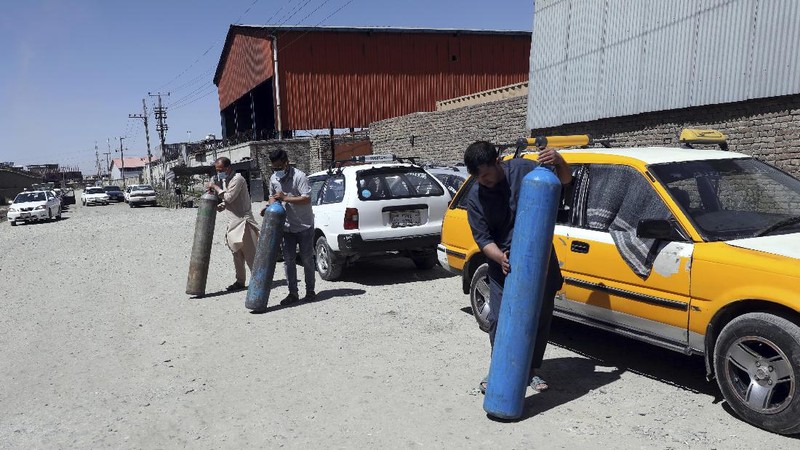A woman carries an oxygen cylinder from a privately owned oxygen factory, in Kabul, Afghanistan, Saturday, June 19, 2021. Health officials say Afghanistan is fast running out of oxygen as a deadly third surge of COVID worsen. (AP Photo/Rahmat Gul)