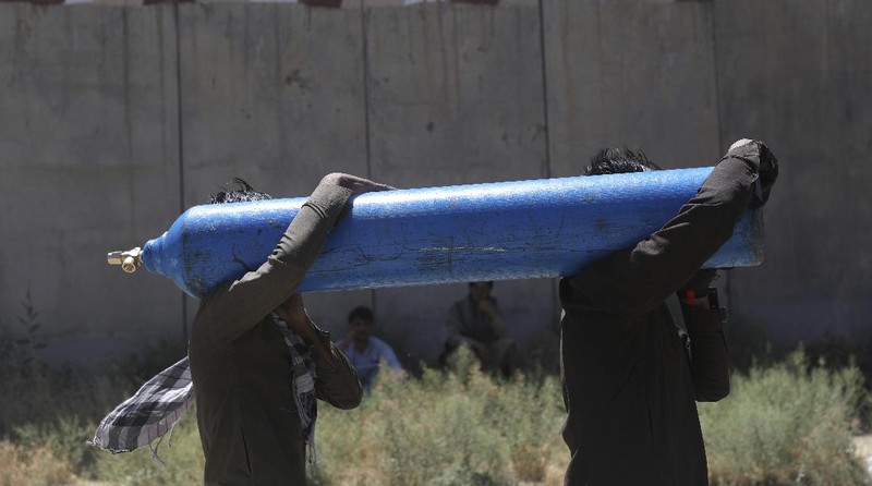 A woman carries an oxygen cylinder from a privately owned oxygen factory, in Kabul, Afghanistan, Saturday, June 19, 2021. Health officials say Afghanistan is fast running out of oxygen as a deadly third surge of COVID worsen. (AP Photo/Rahmat Gul)