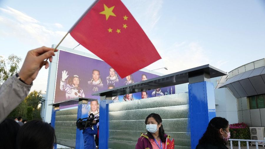 A woman holds up a Chinese flag near a board displaying China's astronauts at the Jiuquan Satellite Launch Center in Jiuquan in northwestern China, Thursday, June 17, 2021. China has launched the first three-man crew to its new space station in its ambitious programs first crewed mission in five years. (AP Photo/Ng Han Guan)