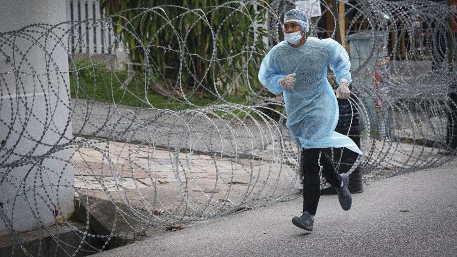 A resident wearing face mask sit outside his house next to barbwire at Segambut Dalam area placed under the enhanced movement control order (EMCO) due to drastic increase in the number of COVID-19 cases recorded over the past 10 days in Kuala Lumpur, Malaysia, Sunday, June 27, 2021. Malaysia's leader says a one-month near total lockdown that is due to end Monday will be extended further as coronavirus infections remain high. (AP Photo/Vincent Thian)