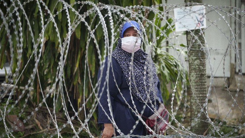 A resident wearing face mask sit outside his house next to barbwire at Segambut Dalam area placed under the enhanced movement control order (EMCO) due to drastic increase in the number of COVID-19 cases recorded over the past 10 days in Kuala Lumpur, Malaysia, Sunday, June 27, 2021. Malaysia's leader says a one-month near total lockdown that is due to end Monday will be extended further as coronavirus infections remain high. (AP Photo/Vincent Thian)