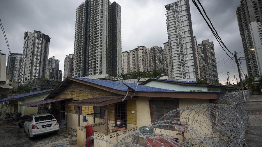 A resident wearing face mask sit outside his house next to barbwire at Segambut Dalam area placed under the enhanced movement control order (EMCO) due to drastic increase in the number of COVID-19 cases recorded over the past 10 days in Kuala Lumpur, Malaysia, Sunday, June 27, 2021. Malaysia's leader says a one-month near total lockdown that is due to end Monday will be extended further as coronavirus infections remain high. (AP Photo/Vincent Thian)