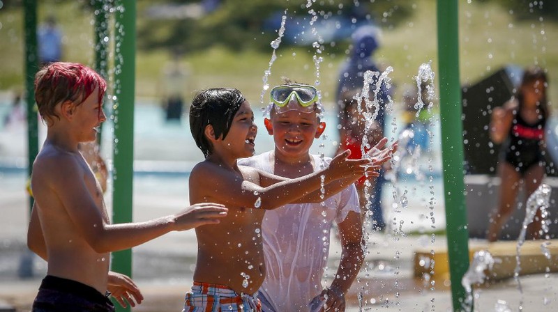 A man stands under a water feature trying to beat the heat at a splash park in Calgary, Alberta, Wednesday, June 30, 2021. Environment Canada warns the torrid heat wave that has settled over much of Western Canada won't lift for days. (Jeff McIntosh/The Canadian Press via AP)