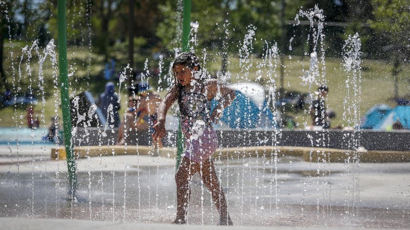 A man stands under a water feature trying to beat the heat at a splash park in Calgary, Alberta, Wednesday, June 30, 2021. Environment Canada warns the torrid heat wave that has settled over much of Western Canada won't lift for days. (Jeff McIntosh/The Canadian Press via AP)