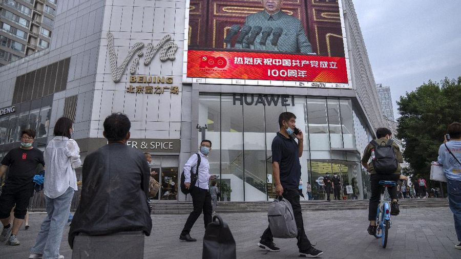 People walk past a large video screen outside a shopping mall showing Chinese President Xi Jinping speaking during an event to commemorate the 100th anniversary of China's Communist Party at Tiananmen Square in Beijing, Thursday, July 1, 2021. China's ruling Communist Party is marking the 100th anniversary of its founding with speeches and grand displays intended to showcase economic progress and social stability to justify its iron grip on political power. (AP Photo/Mark Schiefelbein)