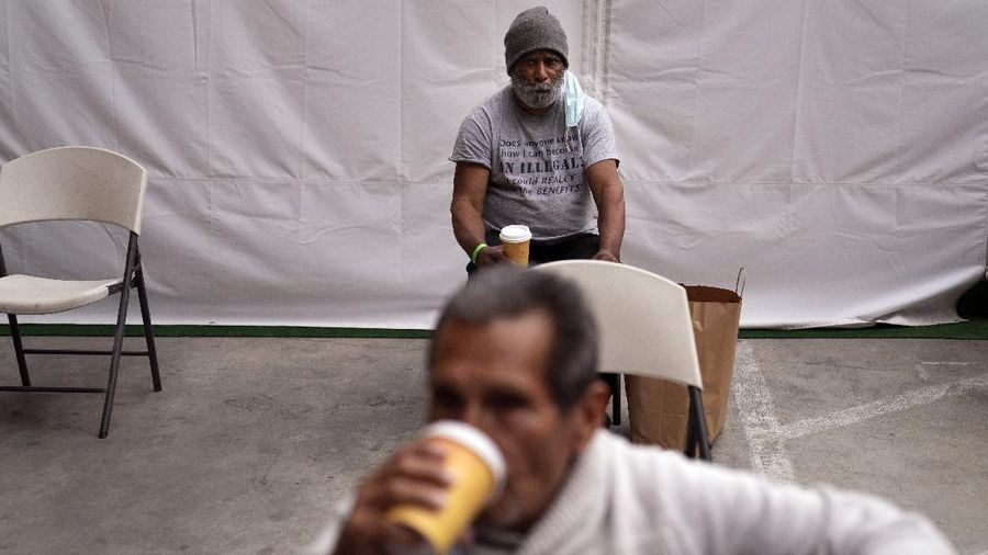 Mark McNamee, a 61-year-old homeless man, and Jesus Huerta, foreground, drink coffee while waiting in the holding area after getting their COVID-19 vaccine at a vaccination site set up in the parking lot of the Los Angeles Mission in the Skid Row area of Los Angeles, Wednesday, Feb. 10, 2021. The vaccine was administered by Los Angeles Department of Health's Housing for Health division for selected individuals, including homeless seniors. (AP Photo/Jae C. Hong)