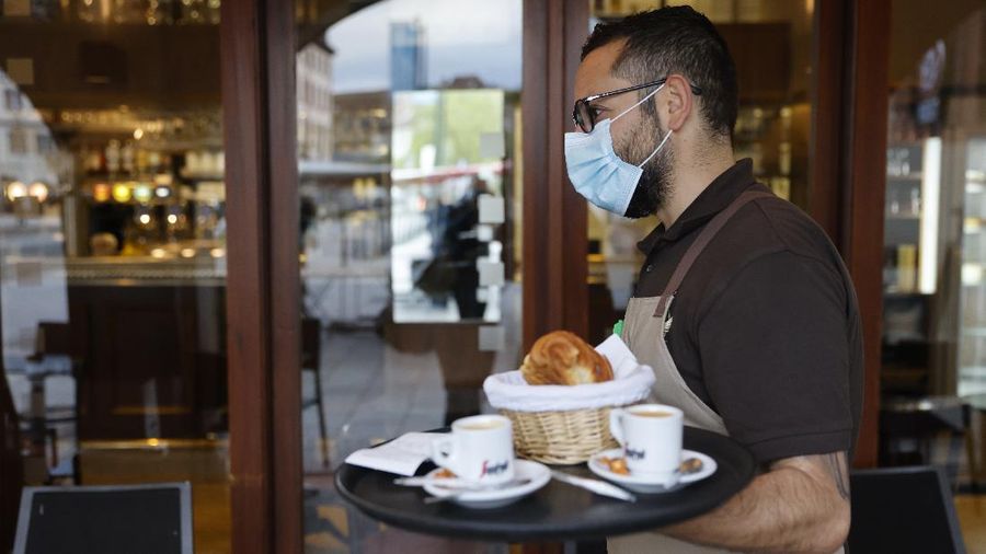 A waiter carries cafes and croissants in a café Wednesday, May, 19, 2021 in Strasbourg, eastern France. It's a grand day for the French. Café and restaurant terraces are reopening Wednesday after a shutdown of more than six months deprived people of what feels like the essence of life — sipping coffee and wine with friends outdoors — to save lives during the coronavirus pandemic. (AP Photo/Jean-Francois Badias)