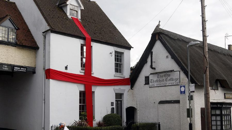 A boy rides by a house decorated with red cloth, to look like the England flag, ahead of the Euro 2020 soccer championship final match between England and Italy to be played at Wembley Stadium on Sunday, in Dunchurch, Warwickshire, England, Saturday, July 10, 2021. (AP Photo/Martin Cleaver)