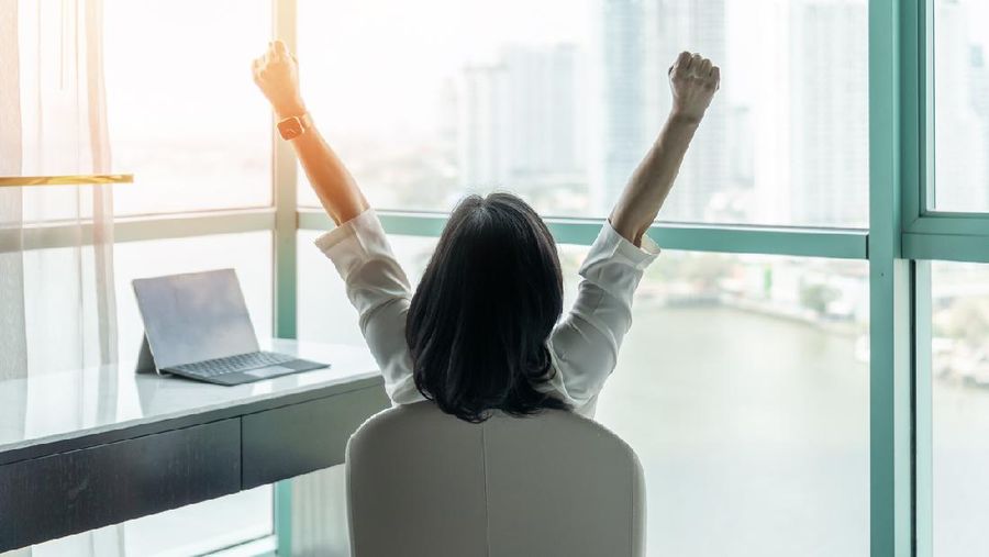 Business achievement concept with happy businesswoman relaxing in office or hotel room, resting and raising fists with ambition looking forward to city building urban scene through glass window