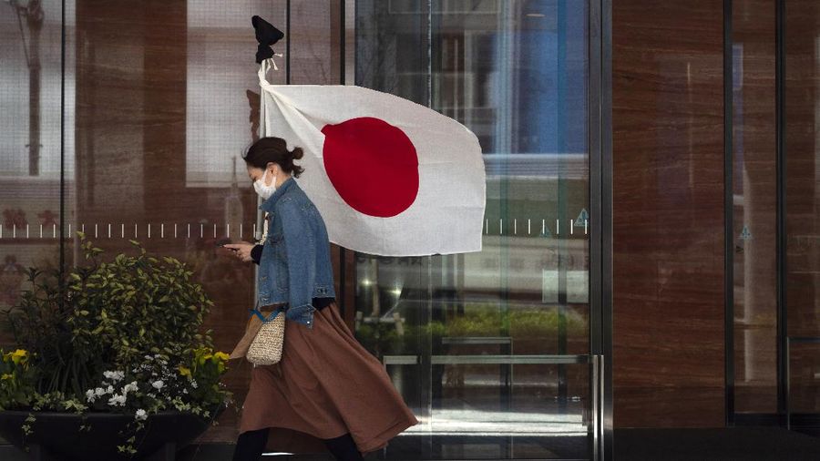 A woman wearing a mask walks past a Japanese flag Wednesday, March 11, 2020, in Tokyo. For most people, the new coronavirus causes only mild or moderate symptoms, such as fever and cough. For some, especially older adults and people with existing health problems, it can cause more severe illness, including pneumonia. The vast majority of people recover from the new virus. (AP Photo/Jae C. Hong)