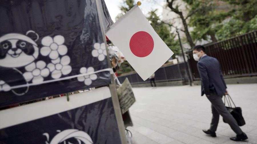A man wearing a protective mask to help curb the spread of the coronavirus walks near a Japanese flag at a shopping arcade at Asakusa district Thursday, Oct. 22, 2020, in Tokyo. (AP Photo/Eugene Hoshiko)