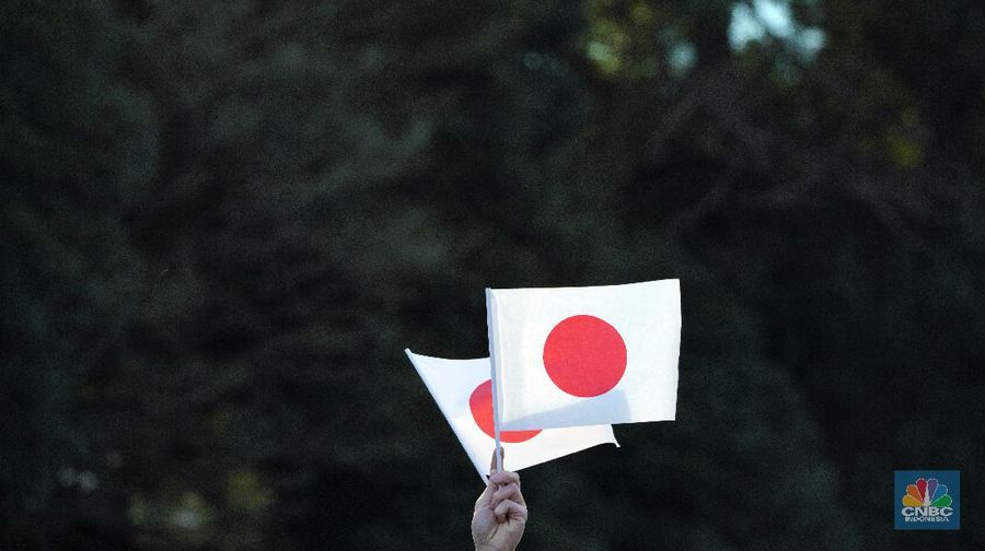 A visitor waves Japanese flags while waiting to see Japan's Emperor Naruhito's New Year public appearance with his imperial families at Imperial Palace in Tokyo Thursday, Jan. 2, 2020, in Tokyo. (AP Photo/Eugene Hoshiko)