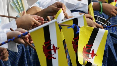 Brunei's Muslim students wait along a road site with Brunei flag's in hands to welcome the sultan for his 60th birthday parade in Bandar Seri Begawan, Brunei,  Saturday, July. 15, 2006. The immensely wealthy Sultan of Brunei celebrated his 60th birthday Saturday, and rewarded his subjects by announcing a pay rise for government employees, the first official increment for the civil service in over two decades. (AP Photo/Vincent Thian)