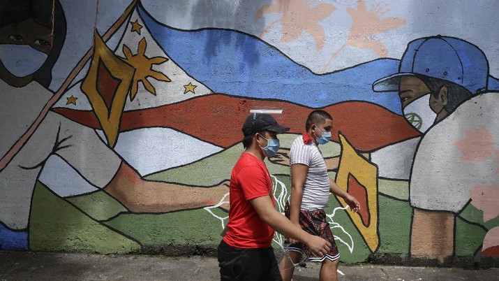 Virus Outbreak Philippines People wearing protective masks to prevent the spread of the coronavirus walk past a mural showing a Philippine flag and Filipinos wearing masks in Manila, Philippines on Wednesday, Oct. 21, 2020. The Philippines lifted a ban on non-essential foreign trips by Filipinos Wednesday but the immigration bureau said the move did not immediately spark large numbers of departures for tourism and leisure. (AP Photo/Aaron Favila)