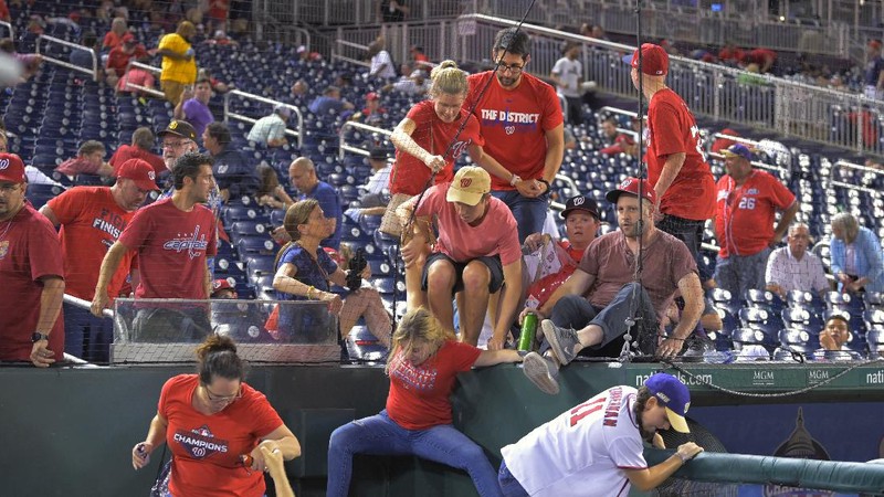 Fans jump into a camera well after hearing gunfire from outside the stadium, during a baseball game between the San Diego Padres and the Washington Nationals at Nationals Park in Washington on Saturday, July 17, 2021. (John McDonnell/The Washington Post via AP)