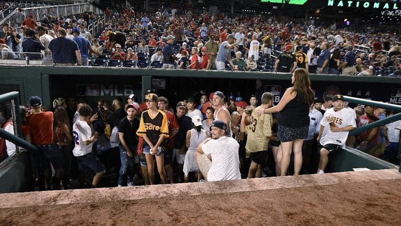 Fans jump into a camera well after hearing gunfire from outside the stadium, during a baseball game between the San Diego Padres and the Washington Nationals at Nationals Park in Washington on Saturday, July 17, 2021. (John McDonnell/The Washington Post via AP)
