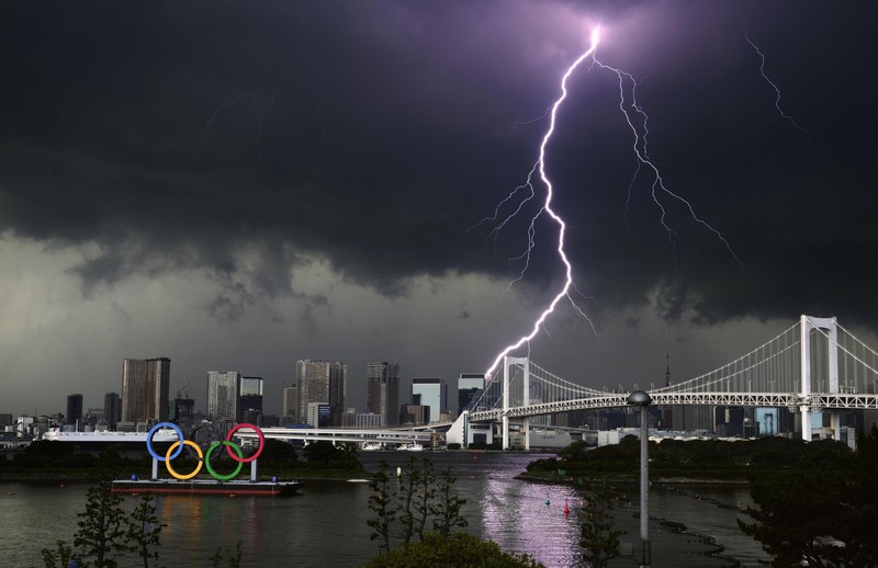 Petir menerangi langit di logo cincin Olimpiade dan Jembatan Pelangi di Tokyo, Minggu, 11 Juli 2021. (Kyodo News via AP) Lightning illuminates the sky over the Olympic rings and the Rainbow Bridge in Tokyo, Sunday, July 11, 2021. The opening ceremony of the postponed 2020 Summer Olympics is scheduled to be held in less than two weeks. (Kyodo News via AP)