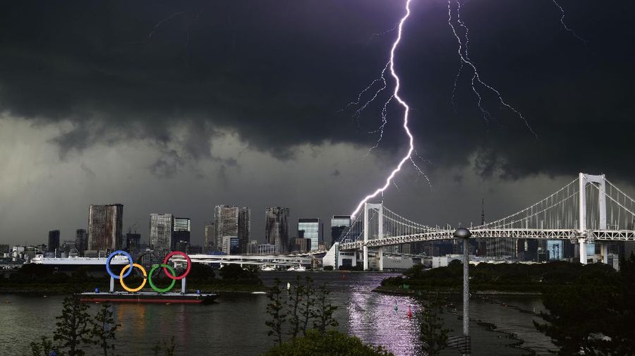 Lightning illuminates the sky over the Olympic rings and the Rainbow Bridge in Tokyo, Sunday, July 11, 2021. The opening ceremony of the postponed 2020 Summer Olympics is scheduled to be held in less than two weeks. (Kyodo News via AP)