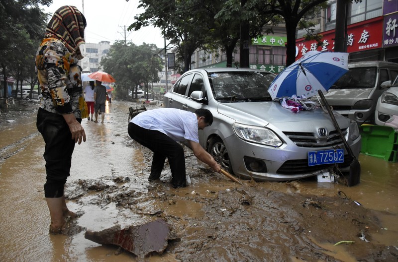 In this photo released by Xinhua News Agency, residents move their belongings across a flooded street in Zhengzhou in central China's Henan province on Wednesday, July 21, 2021. China's military has blasted a dam to release floodwaters threatening one of its most heavily populated provinces, as the death toll in widespread flooding rose to more than two dozens. (Zhu Xiang/Xinhua via AP)