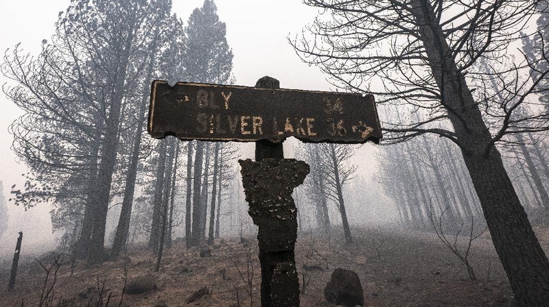 A sign damaged by the Bootleg Fire stands among the haze on Thursday, July 22, 2021, near Paisley, Ore. (AP Photo/Nathan Howard)