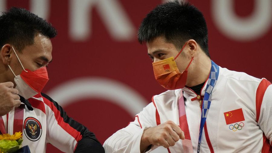 Li Fabin dari China, medali emas (kanan) merayakan di podium dengan peraih medali perak Eko Yuli Irawan dari Indonesia dalam cabang angkat besi 61kg putra di Olimpiade 2020, di Tokyo, Jepang, Minggu, 25 Juli 2021. (AP/Luca Bruno)