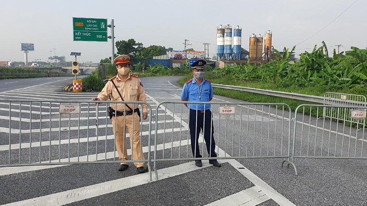 Policemen guard behind barricades set up to control the traffic in Hanoi, Vietnam, Saturday, July 24, 2021. Vietnam announced a 15-day lockdown in the capital Hanoi starting Saturday as a coronavirus surge spread from the southern Mekong Delta region.  (AP Photo/Hieu Dinh)