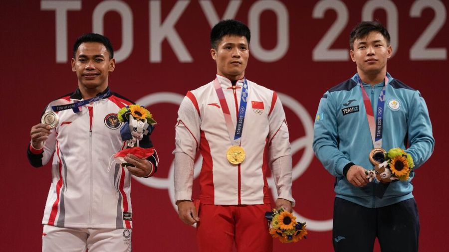 Gold medalist Li Fabin of China, center, stands with silver medalist Eco Yuli Irawan of Indonesia, left, and bronze medalist Igor Son of Kazakhstan, right, after the men's women's kg weightlifting competition in the men's 61kg weightlifting event, at the 2020 Summer Olympics, Sunday, July 25, 2021, in Tokyo, Japan. (AP Photo/Luca Bruno)