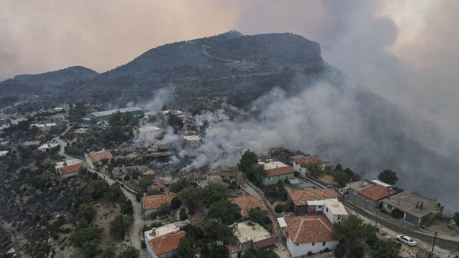 People on the beach of smoke-engulfed Mazi area as wildfires rolled down the hill toward the seashore, in Bodrum, Mugla, Turkey, Sunday, Aug. 1, 2021. More than 100 wildfires have been brought under control in Turkey, according to officials. The forestry minister tweeted that five fires are continuing in the tourist destinations of Antalya and Mugla. (AP Photo/Emre Tazegul)