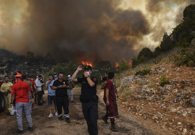 People on the beach of smoke-engulfed Mazi area as wildfires rolled down the hill toward the seashore, in Bodrum, Mugla, Turkey, Sunday, Aug. 1, 2021. More than 100 wildfires have been brought under control in Turkey, according to officials. The forestry minister tweeted that five fires are continuing in the tourist destinations of Antalya and Mugla. (AP Photo/Emre Tazegul)