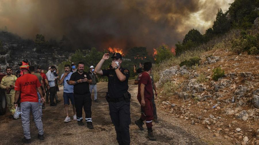People on the beach of smoke-engulfed Mazi area as wildfires rolled down the hill toward the seashore, in Bodrum, Mugla, Turkey, Sunday, Aug. 1, 2021. More than 100 wildfires have been brought under control in Turkey, according to officials. The forestry minister tweeted that five fires are continuing in the tourist destinations of Antalya and Mugla. (AP Photo/Emre Tazegul)