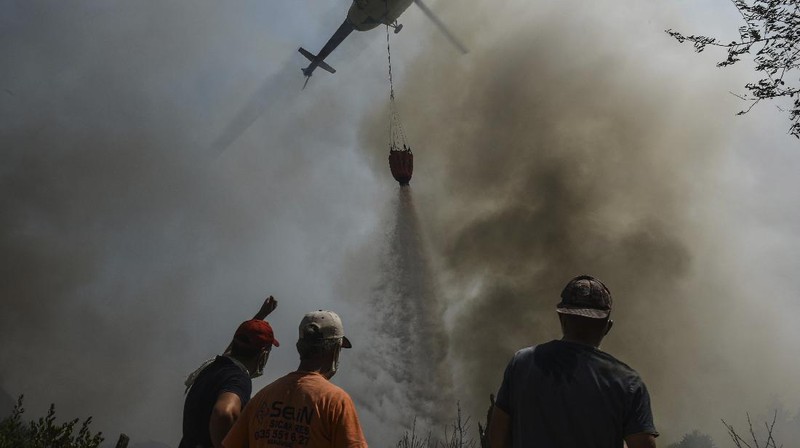 People on the beach of smoke-engulfed Mazi area as wildfires rolled down the hill toward the seashore, in Bodrum, Mugla, Turkey, Sunday, Aug. 1, 2021. More than 100 wildfires have been brought under control in Turkey, according to officials. The forestry minister tweeted that five fires are continuing in the tourist destinations of Antalya and Mugla. (AP Photo/Emre Tazegul)