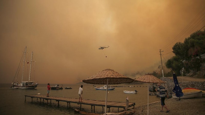 People on the beach of smoke-engulfed Mazi area as wildfires rolled down the hill toward the seashore, in Bodrum, Mugla, Turkey, Sunday, Aug. 1, 2021. More than 100 wildfires have been brought under control in Turkey, according to officials. The forestry minister tweeted that five fires are continuing in the tourist destinations of Antalya and Mugla. (AP Photo/Emre Tazegul)