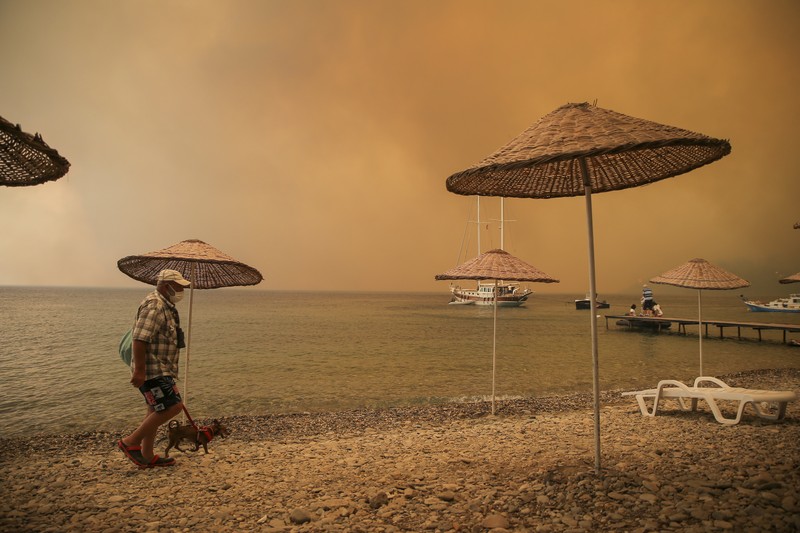 Turkey Wildfire People on the beach of smoke-engulfed Mazi area as wildfires rolled down the hill toward the seashore, in Bodrum, Mugla, Turkey, Sunday, Aug. 1, 2021. More than 100 wildfires have been brought under control in Turkey, according to officials. The forestry minister tweeted that five fires are continuing in the tourist destinations of Antalya and Mugla. (AP Photo/Emre Tazegul)