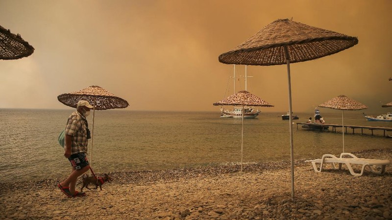 People on the beach of smoke-engulfed Mazi area as wildfires rolled down the hill toward the seashore, in Bodrum, Mugla, Turkey, Sunday, Aug. 1, 2021. More than 100 wildfires have been brought under control in Turkey, according to officials. The forestry minister tweeted that five fires are continuing in the tourist destinations of Antalya and Mugla. (AP Photo/Emre Tazegul)