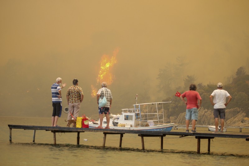 Turkey Wildfire People on the beach of smoke-engulfed Mazi area as wildfires rolled down the hill toward the seashore, in Bodrum, Mugla, Turkey, Sunday, Aug. 1, 2021. More than 100 wildfires have been brought under control in Turkey, according to officials. The forestry minister tweeted that five fires are continuing in the tourist destinations of Antalya and Mugla. (AP Photo/Emre Tazegul)