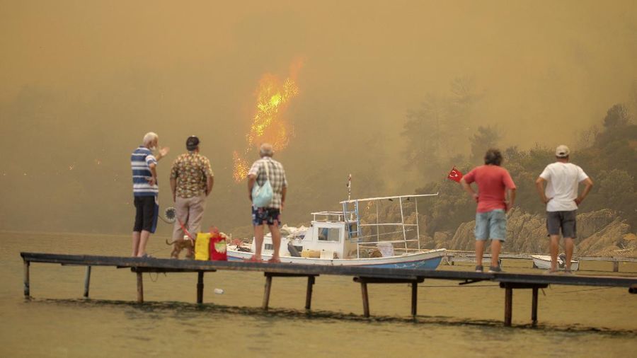 People on the beach of smoke-engulfed Mazi area as wildfires rolled down the hill toward the seashore, in Bodrum, Mugla, Turkey, Sunday, Aug. 1, 2021. More than 100 wildfires have been brought under control in Turkey, according to officials. The forestry minister tweeted that five fires are continuing in the tourist destinations of Antalya and Mugla. (AP Photo/Emre Tazegul)