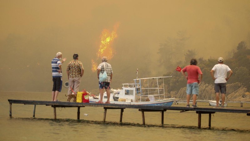 People on the beach of smoke-engulfed Mazi area as wildfires rolled down the hill toward the seashore, in Bodrum, Mugla, Turkey, Sunday, Aug. 1, 2021. More than 100 wildfires have been brought under control in Turkey, according to officials. The forestry minister tweeted that five fires are continuing in the tourist destinations of Antalya and Mugla. (AP Photo/Emre Tazegul)