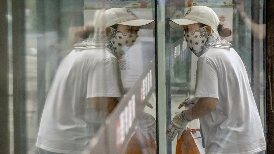 A delivery courier wearing a face mask to protect against COVID-19 is reflected in a window glass as she walks into a restaurant in Beijing, Tuesday, July 27, 2021. (AP Photo/Mark Schiefelbein)