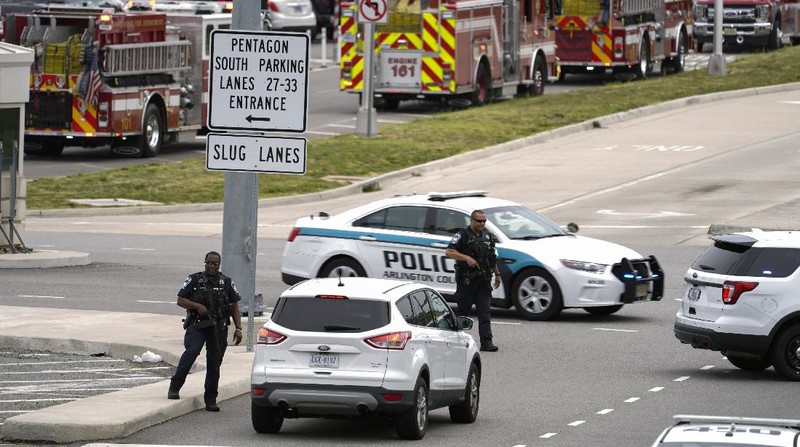 A police officer looks at a vehicle outside the Pentagon, Tuesday, Aug. 3, 2021 in Washington. Gunshots were fired Tuesday morning near the entrance of the Pentagon, resulting in multiple injuries. The facility, the headquarters of the U.S. military, was placed on lockdown. The incident occurred on a Metro bus platform that is part of the Pentagon Transit Center, the Pentagon Protection Force Protection Agency tweeted. (AP Photo/Andrew Harnik)