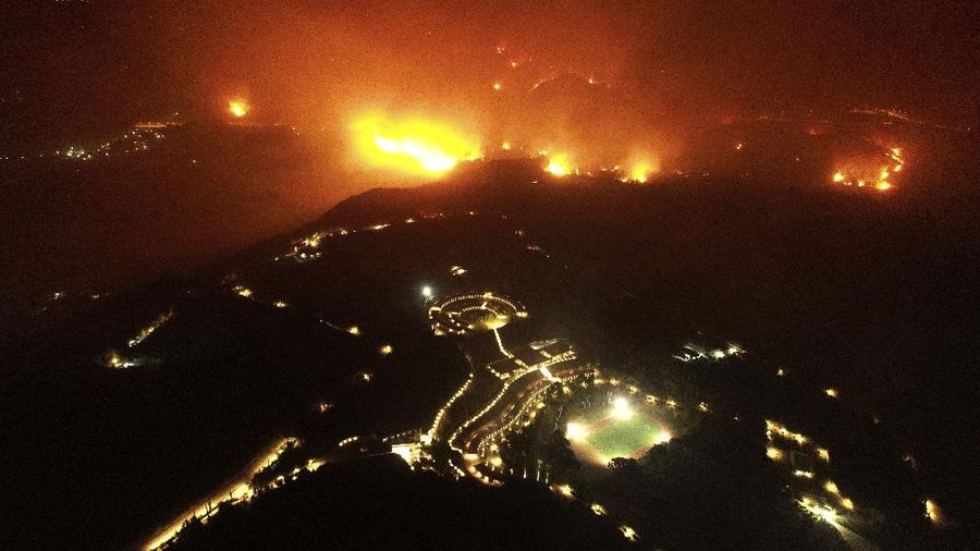 A wildfire approaches the Olympic Academy, foreground, in ancient Olympia, Wednesday, Aug. 4, 2021. Greece evacuated people in boats from an island beach Wednesday amid heavy smoke from a nearby wildfire and fire crews fought elsewhere to keep flames away from the birthplace of the ancient Olympic Games as the country sweltered under a record heat wave. (Giannis Spyrounis/ilialive.gr via AP)
