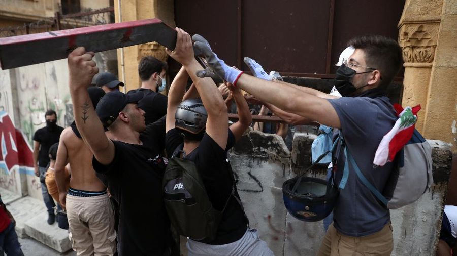 An anti-government protester flashes the victory sign amid tear gas fired by riot police during a protest marking the first anniversary of the massive blast at Beirut's port, near Parliament Square, In Beirut, Lebanon, Wednesday, Aug. 4, 2021. United in grief and anger, families of the victims and other Lebanese came out into the streets of Beirut on Wednesday to demand accountability as banks, businesses and government offices shuttered to mark one year since the horrific explosion. (AP Photo/Bilal Hussein)