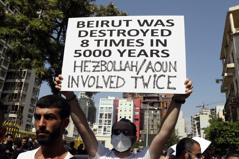 An anti-government protester flashes the victory sign amid tear gas fired by riot police during a protest marking the first anniversary of the massive blast at Beirut's port, near Parliament Square, In Beirut, Lebanon, Wednesday, Aug. 4, 2021. United in grief and anger, families of the victims and other Lebanese came out into the streets of Beirut on Wednesday to demand accountability as banks, businesses and government offices shuttered to mark one year since the horrific explosion. (AP Photo/Bilal Hussein)